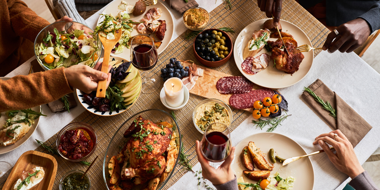 Menschen sitzen am weihnachtlich gedeckten Tisch mit Gänsebraten, Wurstplatte und Beilagen